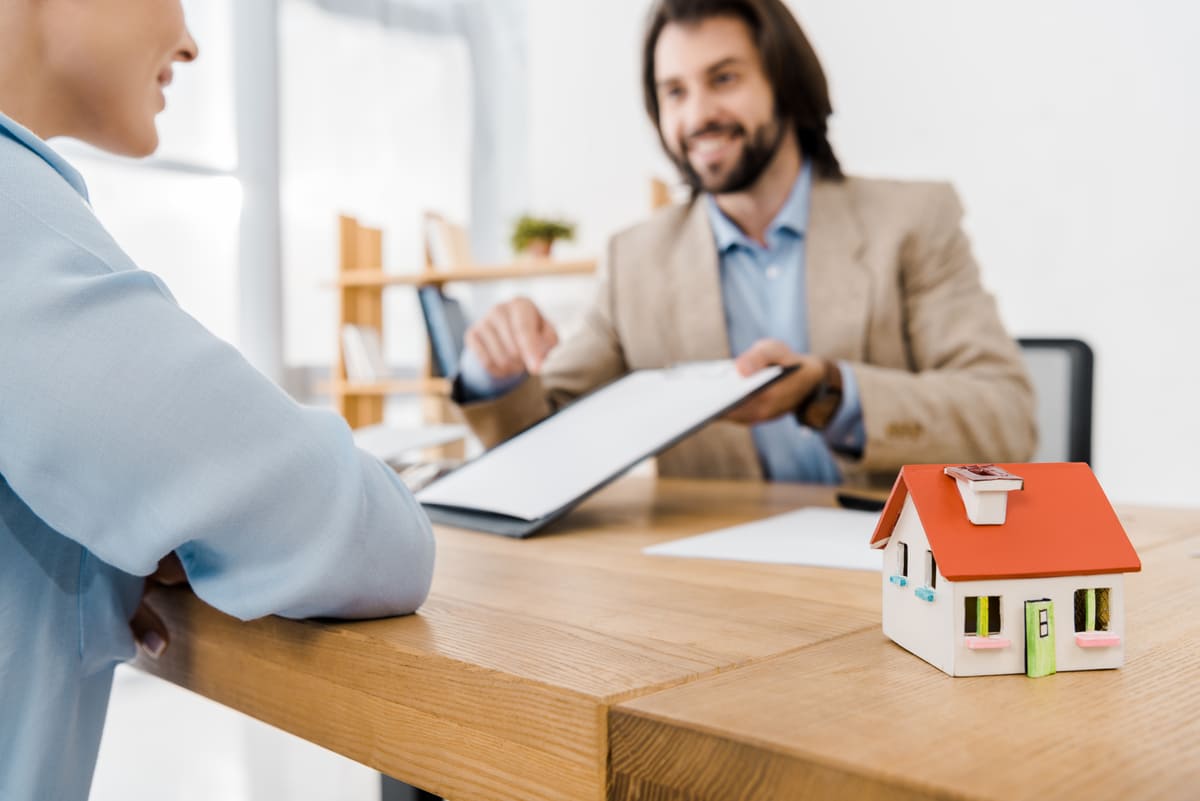 A man smiling and going over a contract with a woman next to a small home