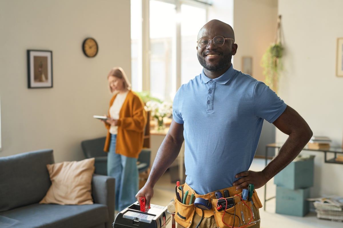 A smiling man with a tool belt and toolbox in a home