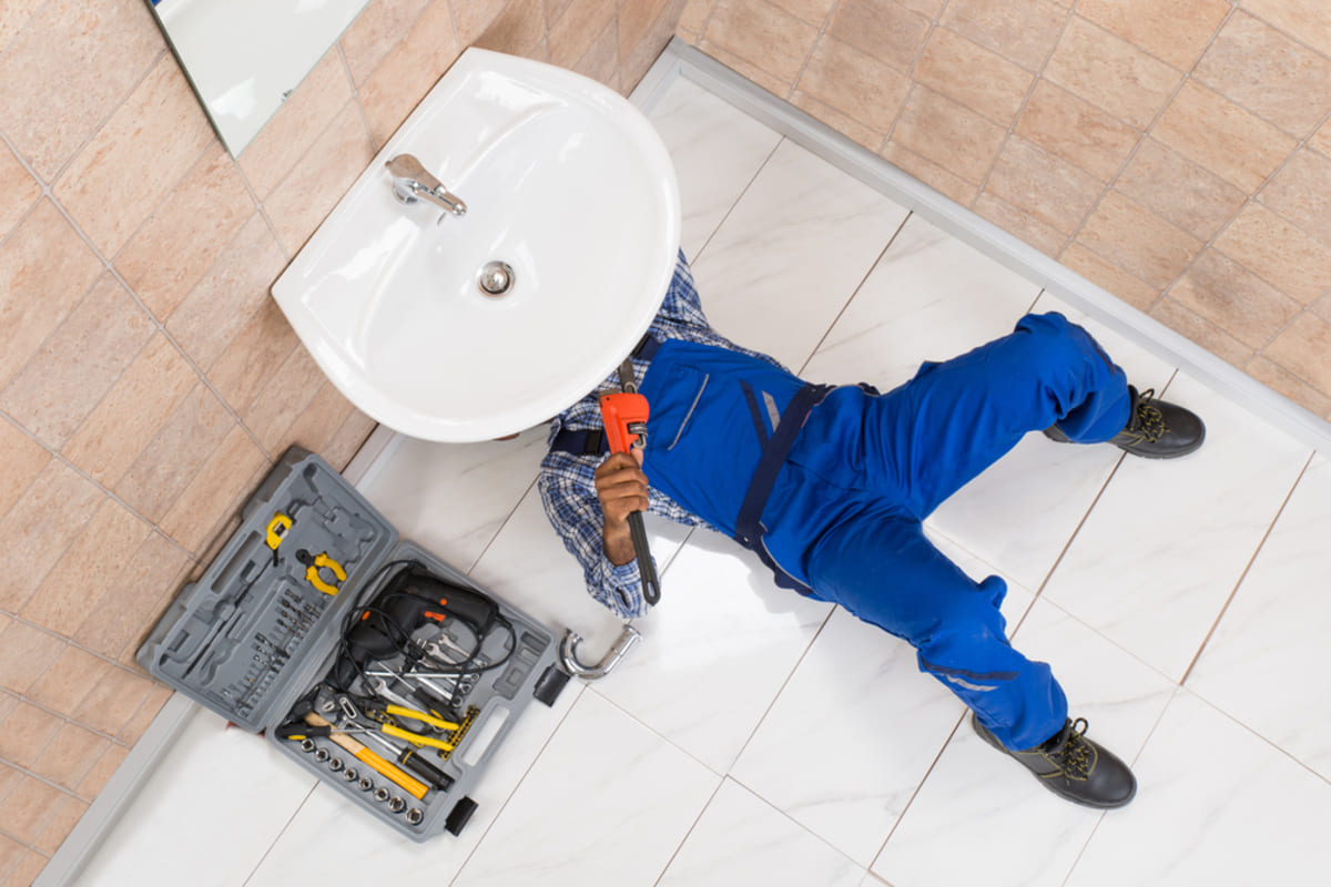 A worker fixing something under a sink, rental property maintenance concept