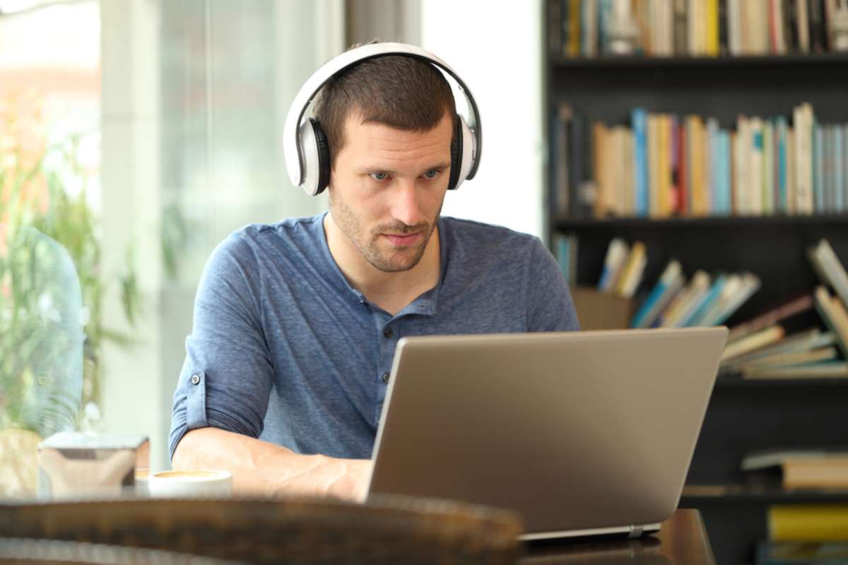 Adult man wearing headphones using a laptop e-learning in a coffee shop or home