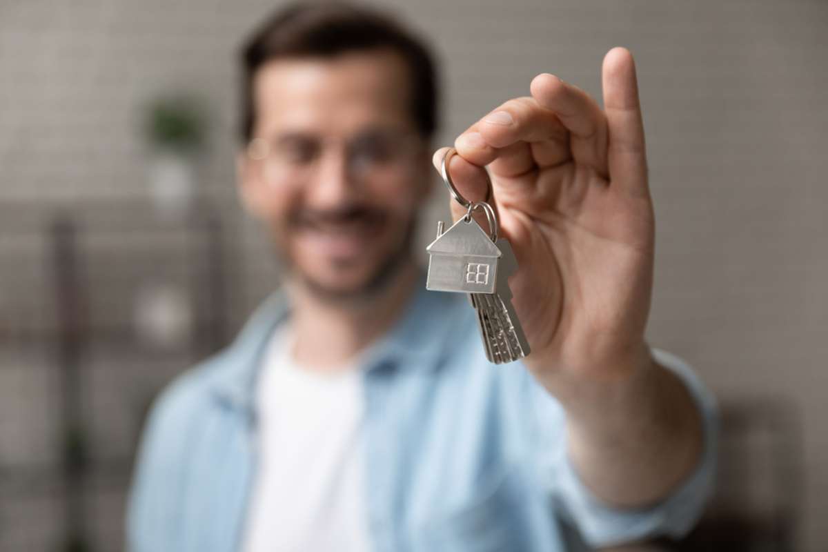 Blurred portrait of happy young man buyer renter of new modern home apartment holding key demonstrating wellbeing wealth celebrate achievement