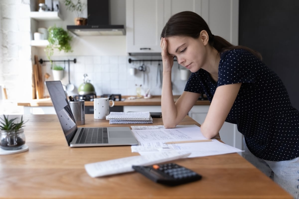 Concerned young woman thinking over domestic paperwork, sitting at laptop computer