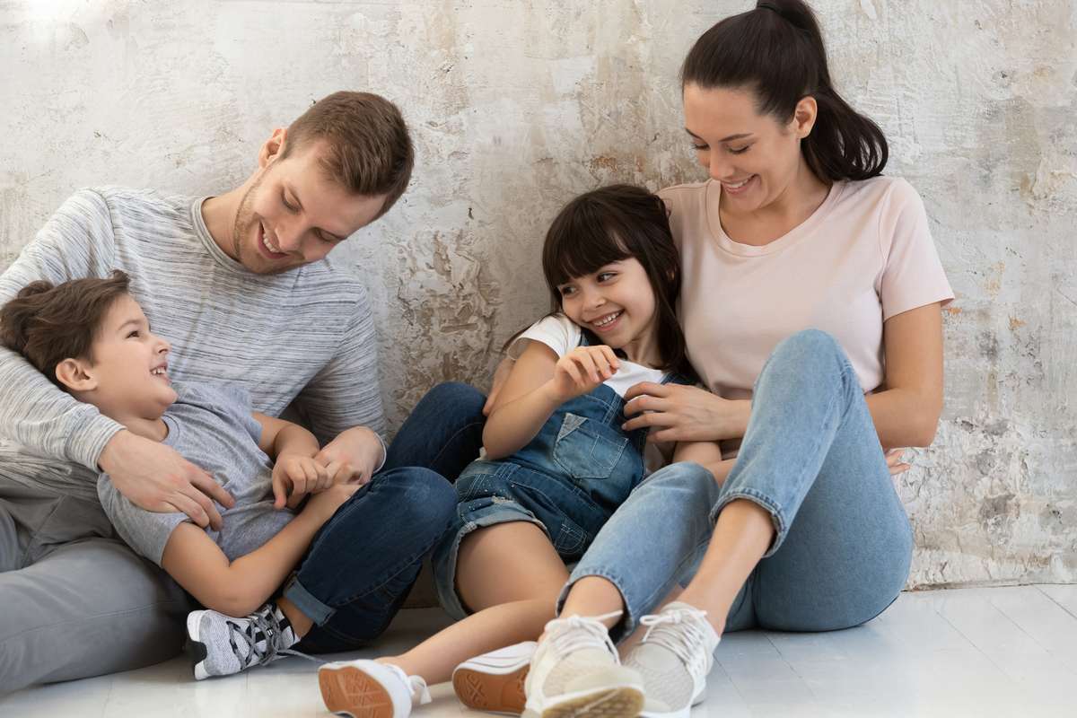 Happy parents and cute children playing tickling sit on floor
