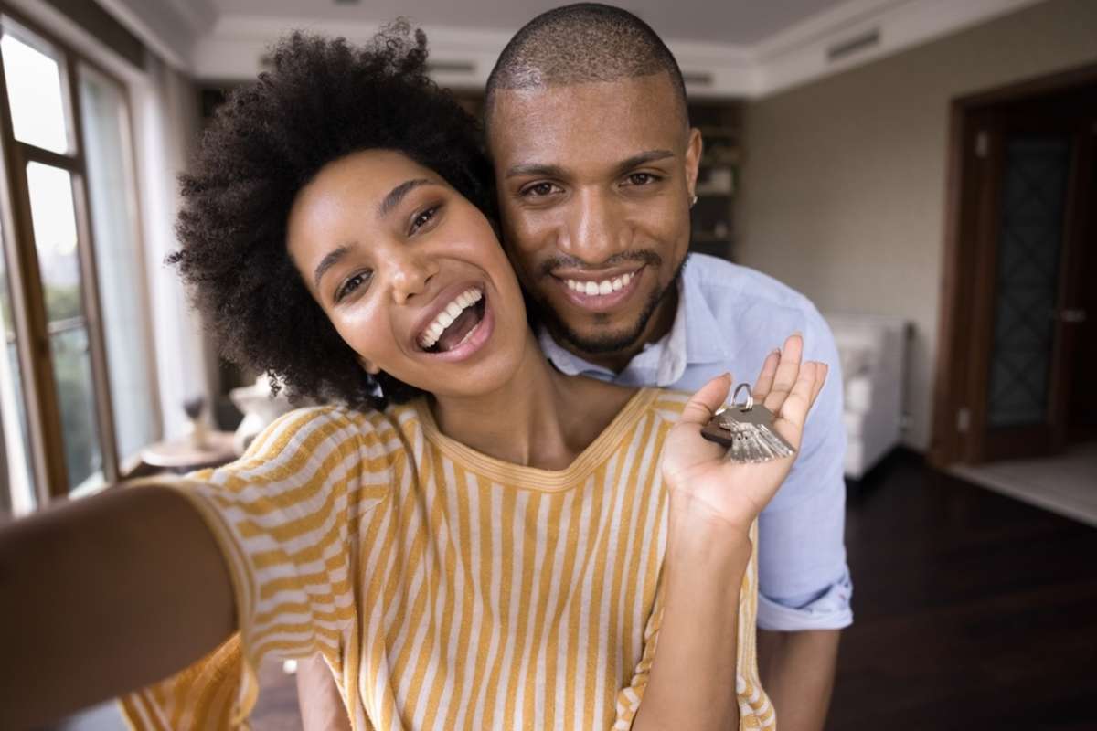 Joyful emotional bonding young african american married couple showing keys to camera