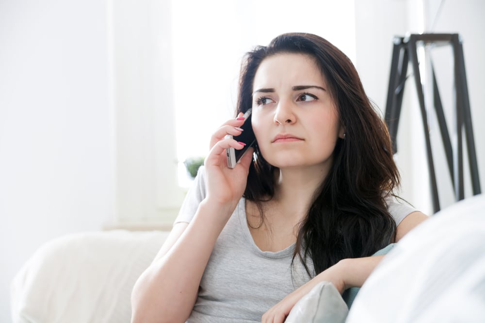 Unhappy worried woman talking on phone while sitting on sofa