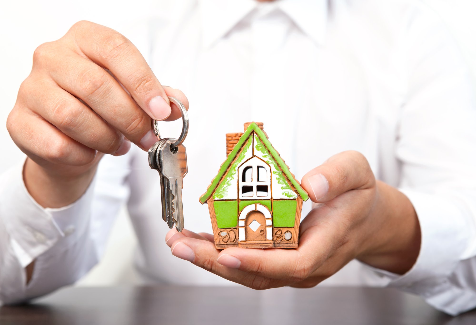 Businessman holding a small house and apartment keys in hand