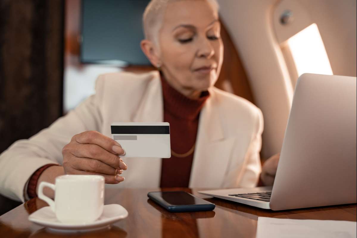 Credit card in hand of blurred businesswoman using laptop near coffee in plane (R) (S)