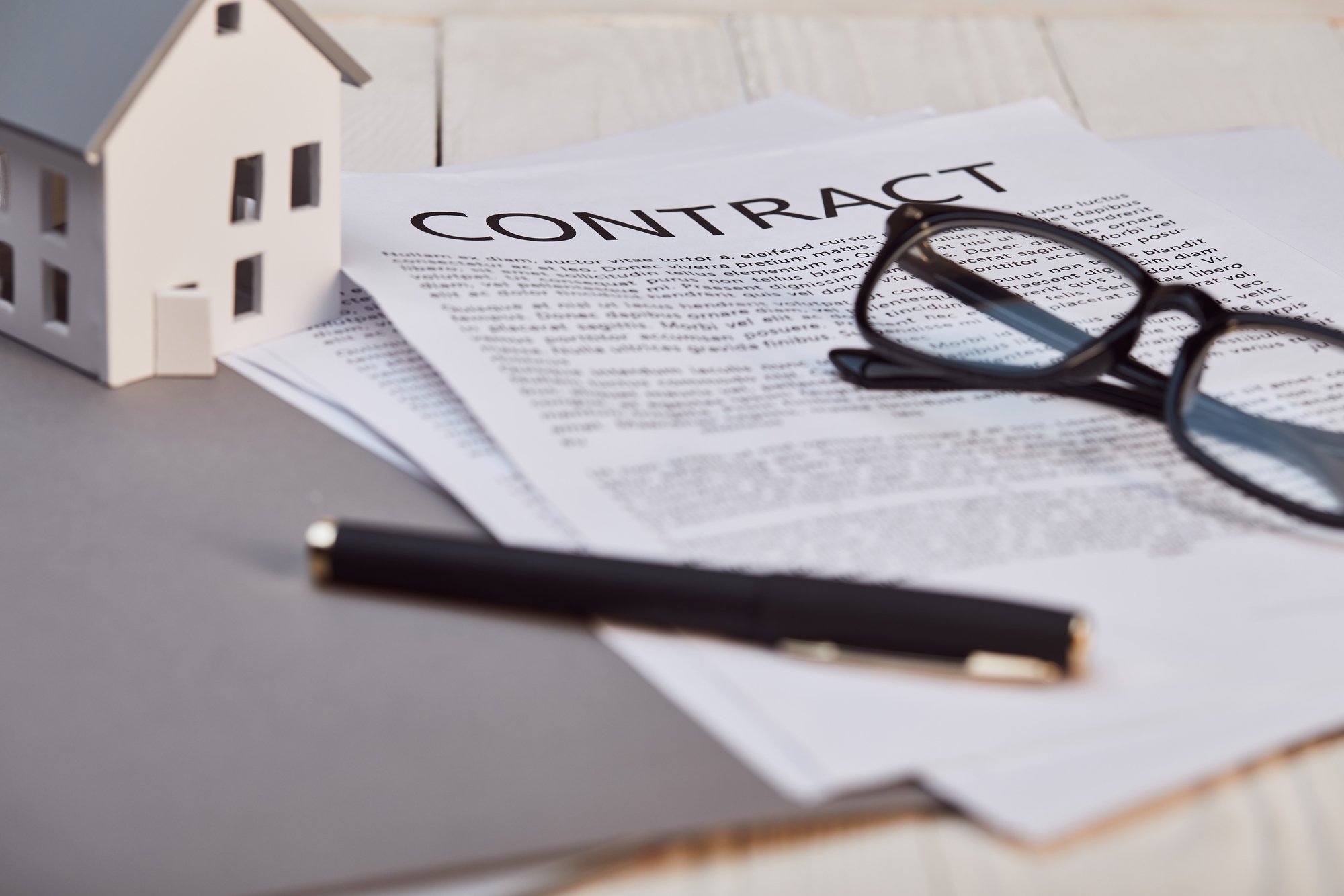 House model on white wooden table near contract and glasses, real estate concept