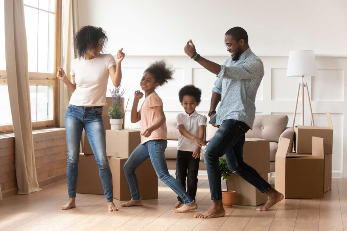 Happy african american parents and cute children dancing among boxes celebrating moving day relocation renovation