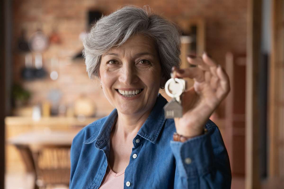 Head shot portrait smiling mature woman holding key from new home