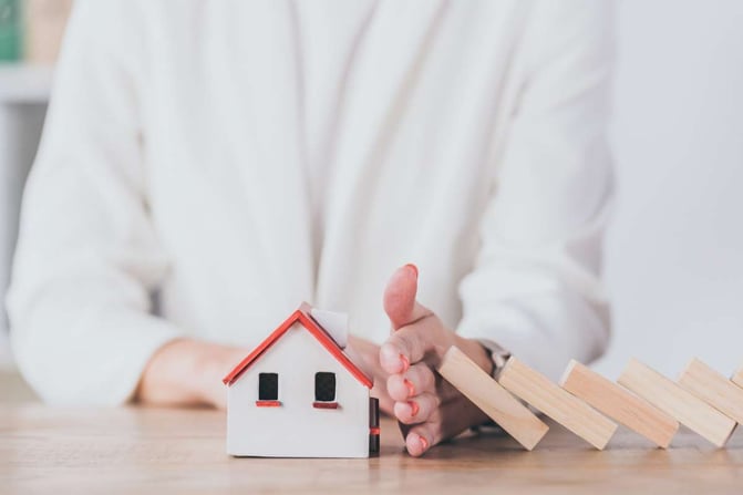 Partial view of risk manager protecting house model from falling wooden blocks with hand
