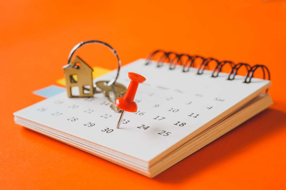 red thumbtack marked the last day of month on white calendar with blurred mini house and key on vivid grunge paper background