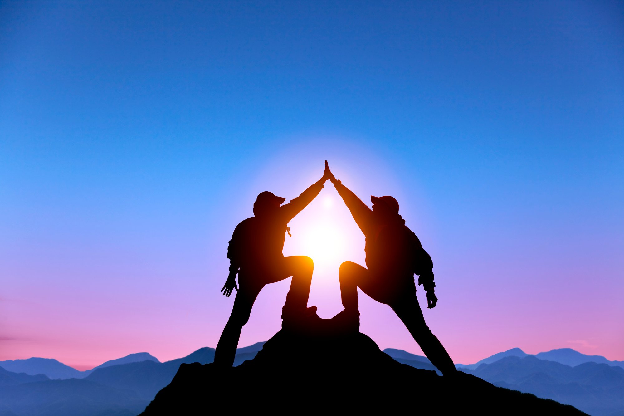 The Silhouette of two man with success gesture standing on the top of mountain