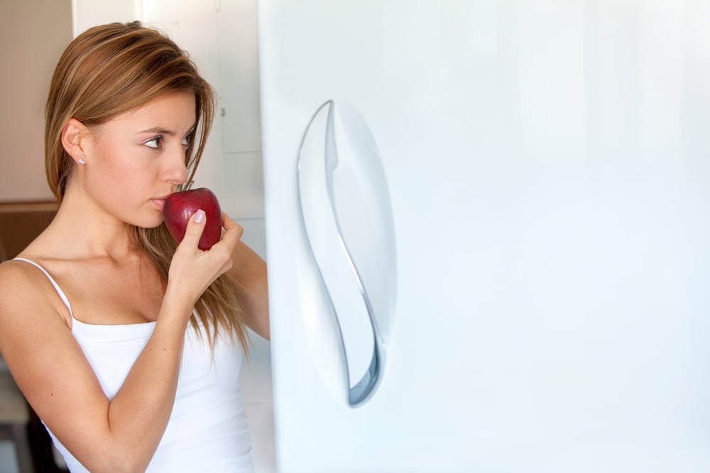 Woman opening the fridge and eating an apple