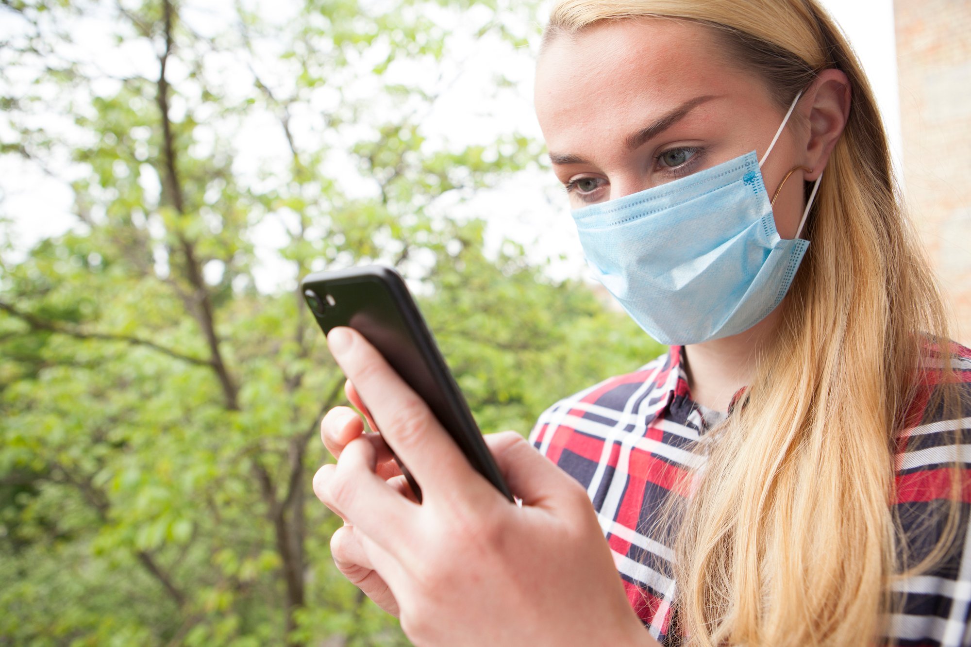 Young woman wearing medical mask outdoors, using her smart phone