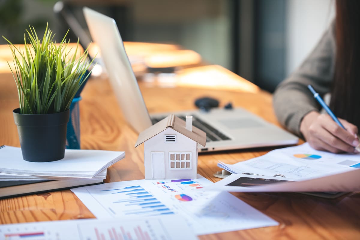 A small house on a table next to charts, graphs and contracts