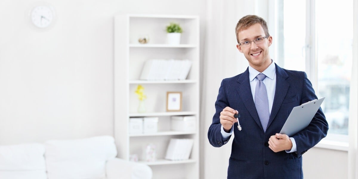 A man in a suit holding keys and a clipboard in a home