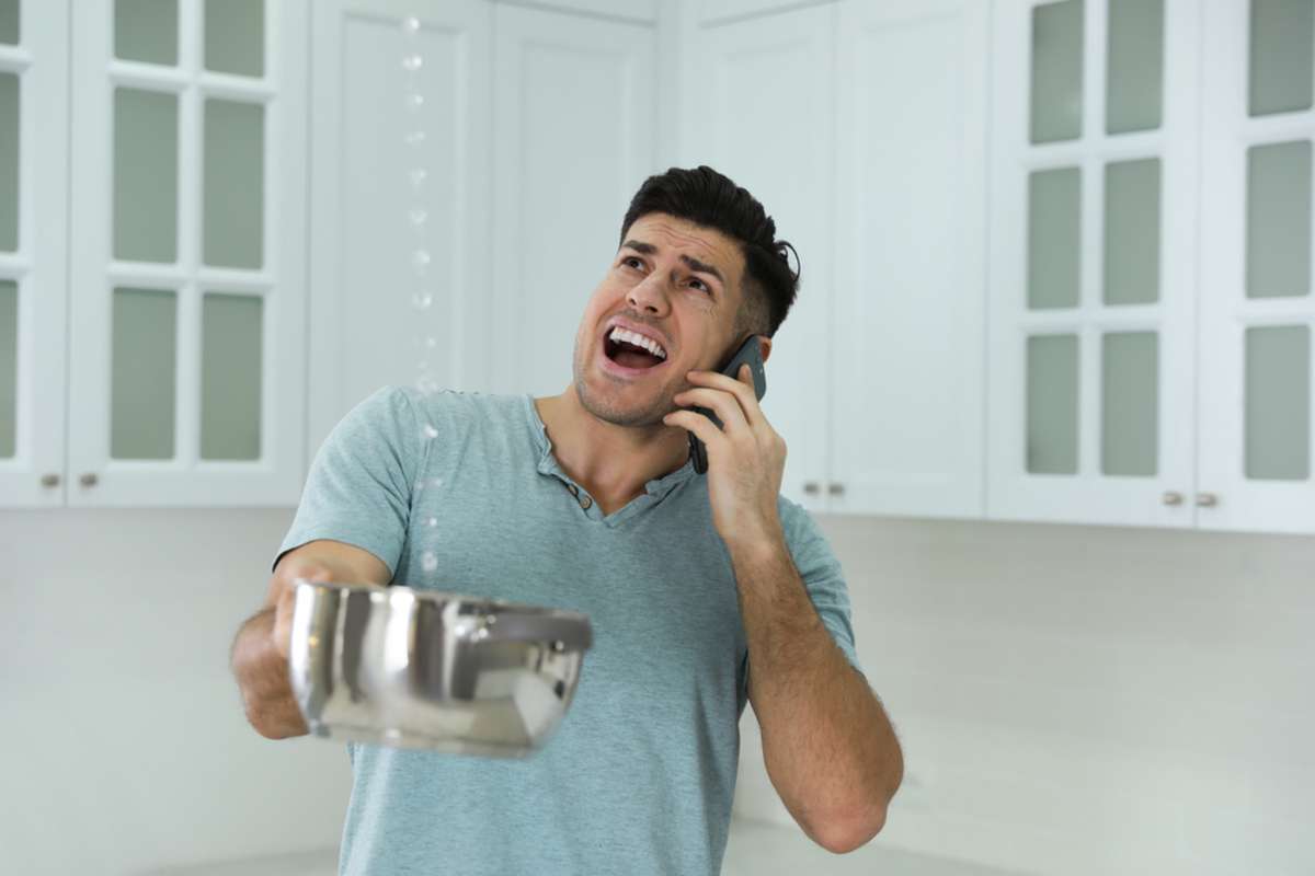 Man holds a pot to catch water from a roof leak, an emergency maintenance issue