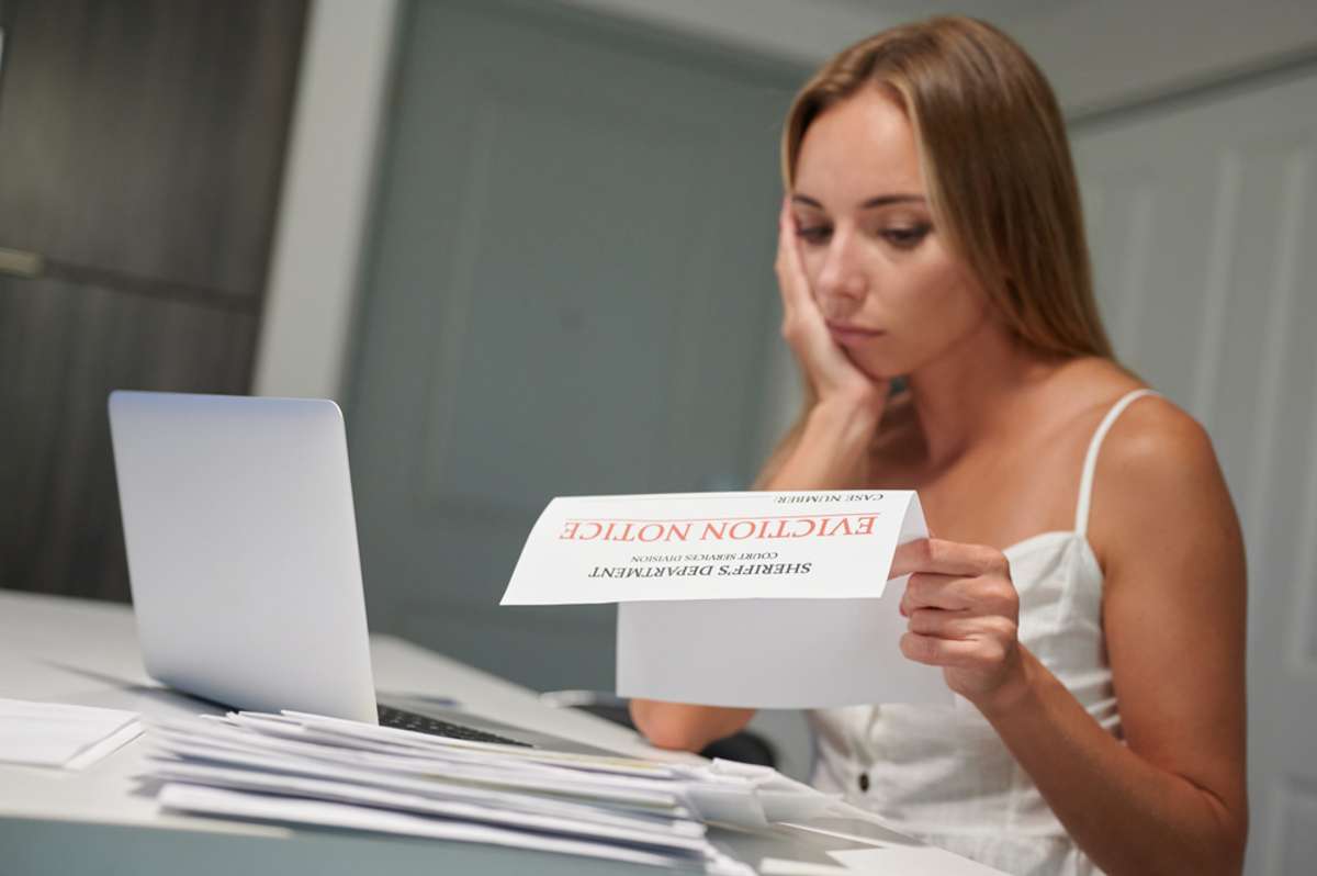 Worried young female with laptop reading eviction letter